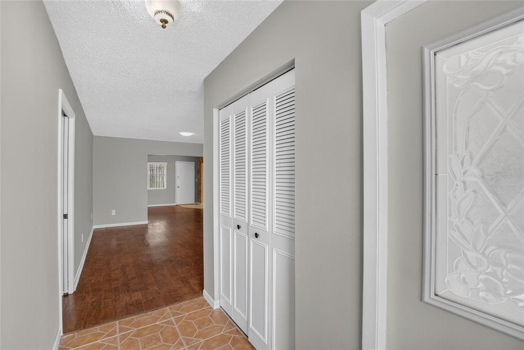 A hallway with tiled flooring leads to a living area with wood-look floors and closets — 1244 W DEL WEBB BOULEVARD, SUN CITY CENTER, FL