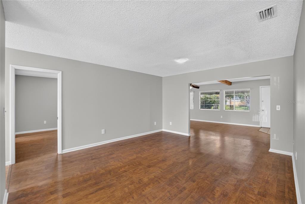 An empty living room features gray walls, wood-look flooring, and an open doorway to another room — 1244 W DEL WEBB BOULEVARD, SUN CITY CENTER, FL
