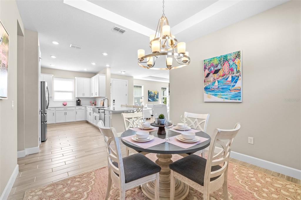 A dining area with a round table and chandelier opens into a white kitchen — 4639 GAROFALO ROAD, WESLEY CHAPEL, FL
