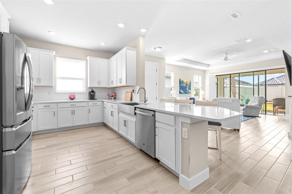 A modern kitchen with white cabinets, quartz countertops, and stainless steel appliances opens to a living area — 4639 GAROFALO ROAD, WESLEY CHAPEL, FL