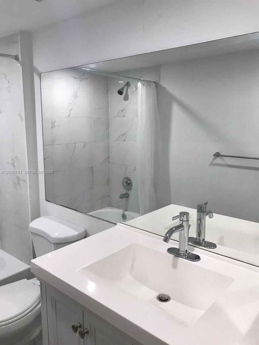 A doorway opens into a bathroom featuring gray floor tiles and a white tiled shower — 462 NE 210th Cir Ter # 9, Miami FL 33179, MIAMI, FL