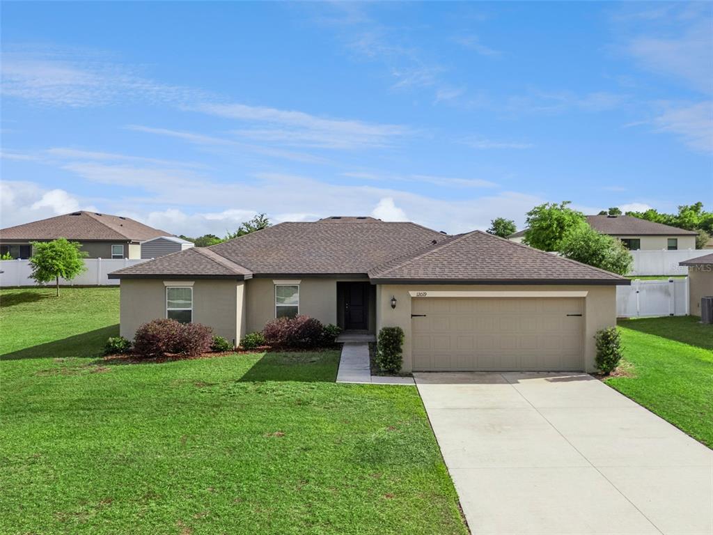 A single-story house with a tan stucco exterior, a brown roof, and a two-car garage — 12019 INDIAN GRASS WAY, LEESBURG, FL