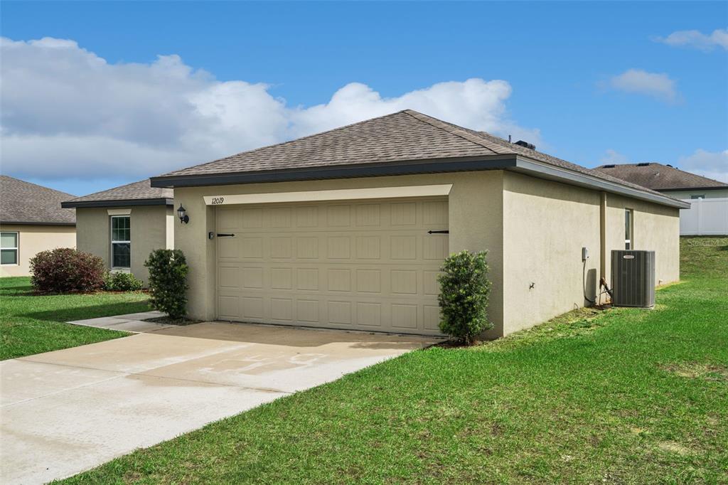 A beige single-story house features a two-car garage, a concrete driveway, and a grassy lawn — 12019 INDIAN GRASS WAY, LEESBURG, FL