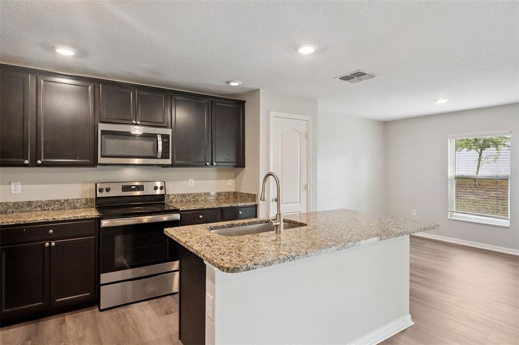 A kitchen features dark wood cabinets, granite countertops, stainless steel appliances, and a center island — 12019 INDIAN GRASS WAY, LEESBURG, FL