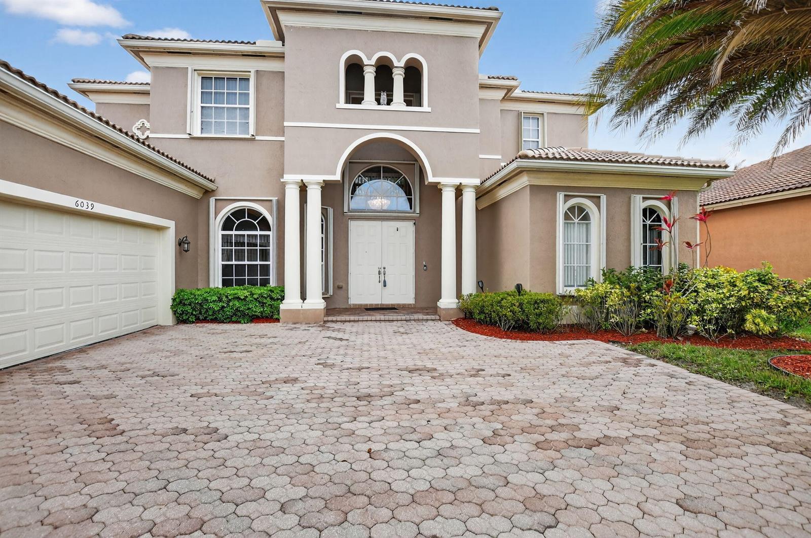 A two-story house with a beige stucco exterior, arched windows, and a paved driveway — 6039 Walnut Hill Drive, Lake Worth FL 33467, LAKE WORTH, FL
