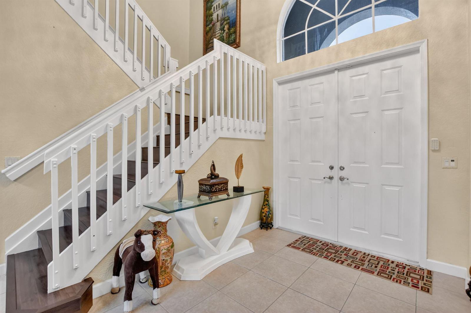 A foyer features a white double door, a staircase with dark treads, and a glass console — 6039 Walnut Hill Drive, Lake Worth FL 33467, LAKE WORTH, FL