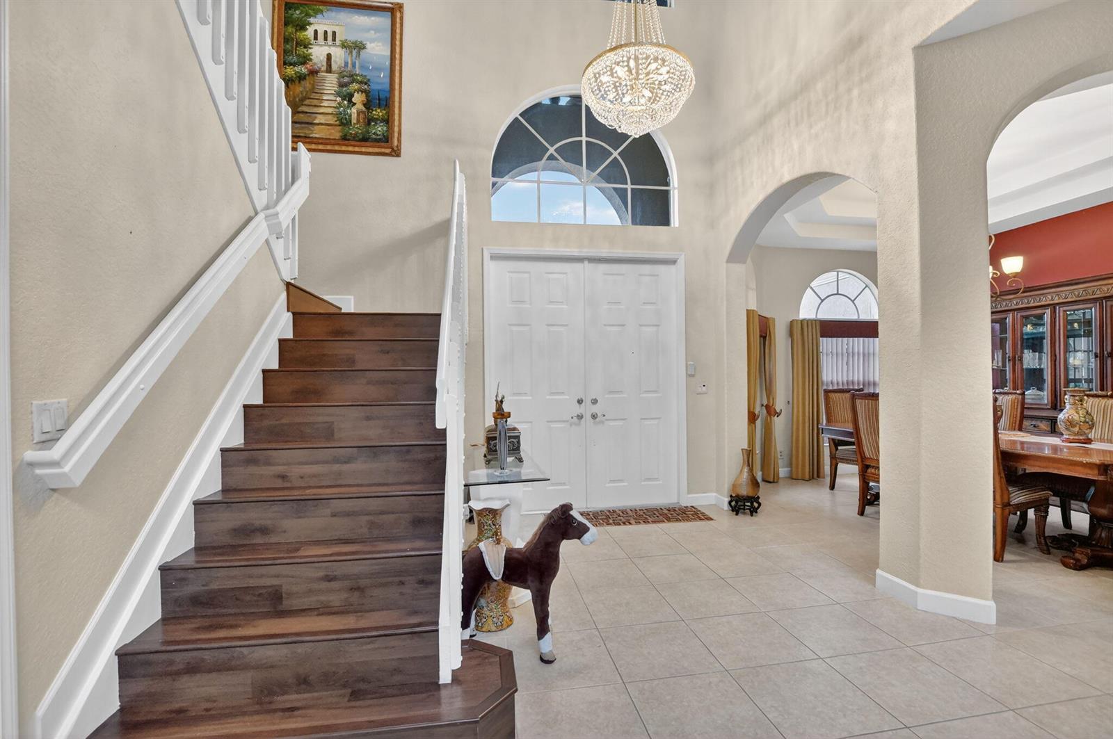 A foyer features a wooden staircase, a crystal chandelier, and a view into a dining room — 6039 Walnut Hill Drive, Lake Worth FL 33467, LAKE WORTH, FL