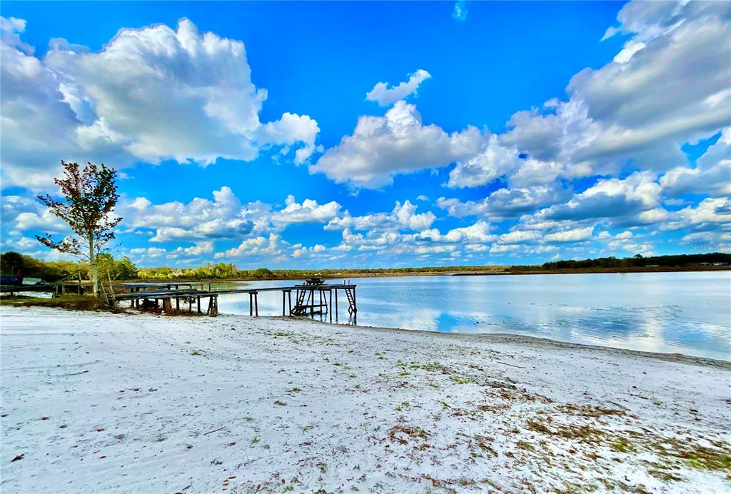 A sandy beach leads to a wooden dock extending into a calm lake under clouds — 106 E SUNNYSIDE BEACH ROAD, HAWTHORNE, FL