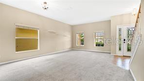 A spacious living room with beige walls, light carpeting, and a glass-paneled front door — 9068 VICKROY TERRACE, OVIEDO, FL