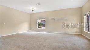A spacious, carpeted room features beige walls, a window, and floating shelves — 9068 VICKROY TERRACE, OVIEDO, FL