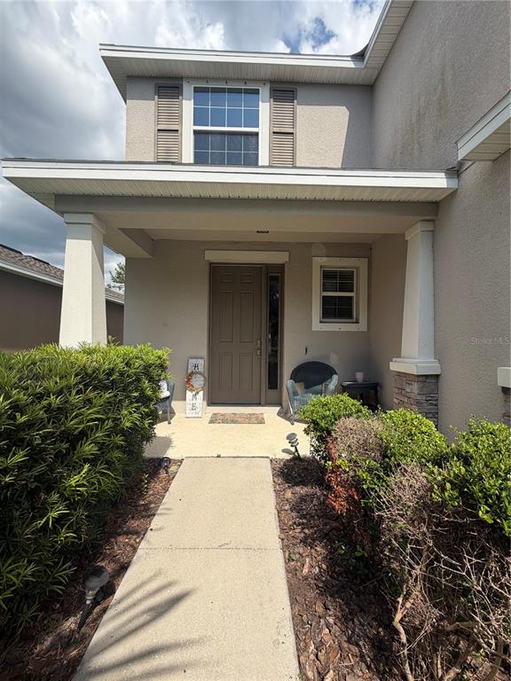 A tan two-story house features a covered front porch, a brown door, and landscaping — 6305 SUNSAIL PLACE, APOLLO BEACH, FL