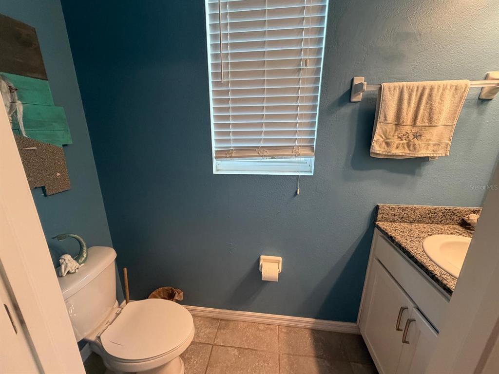 A bathroom features blue walls, a white toilet, a vanity with a granite countertop, and blinds — 6305 SUNSAIL PLACE, APOLLO BEACH, FL