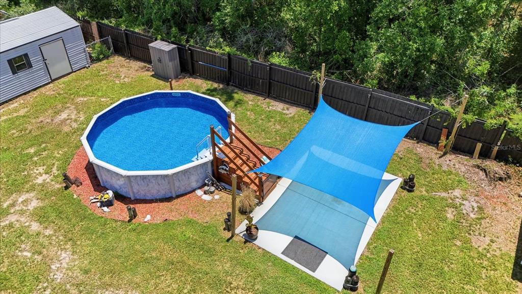 An aerial view of a backyard featuring an above-ground pool, wooden deck, and shade sail — 7606 E SAVANNAH DRIVE, FLORAL CITY, FL