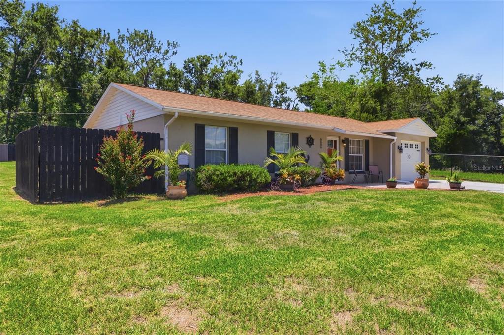 A single-story house with a tan exterior, dark shutters, and a black wooden privacy fence — 7606 E SAVANNAH DRIVE, FLORAL CITY, FL