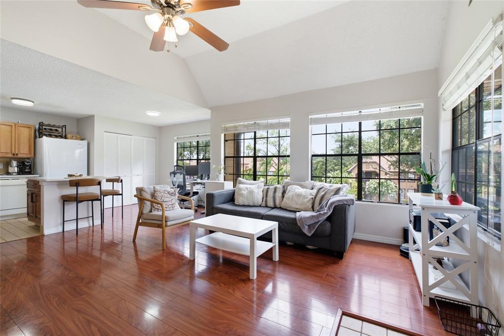 A living room with hardwood floors, a vaulted ceiling, and large windows overlooking trees — 364 NORTHPOINTE COURT UNIT 208, ALTAMONTE SPRINGS, FL