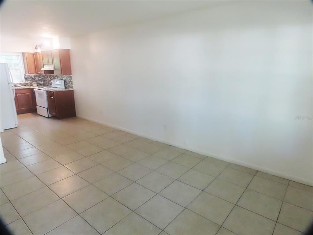 An open-concept dining area with beige tile flooring leads into a kitchen with wood cabinets — 1307 COOK STREET, DELAND, FL