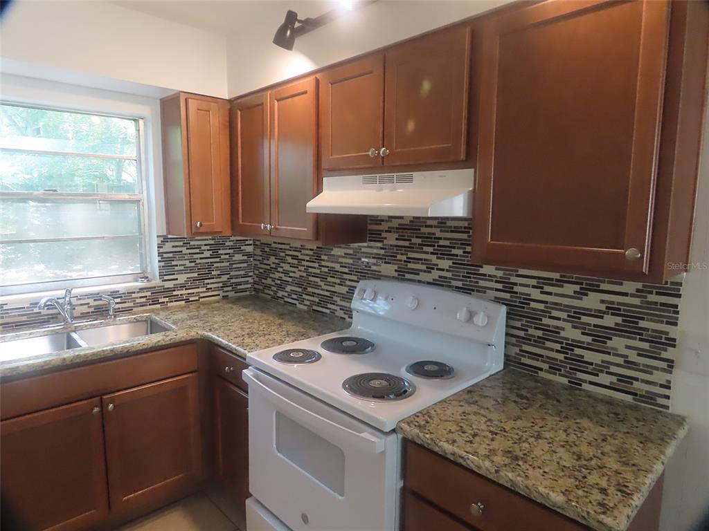 A kitchen features wood cabinets, granite countertops, a white stove, and a mosaic tile backsplash — 1307 COOK STREET, DELAND, FL