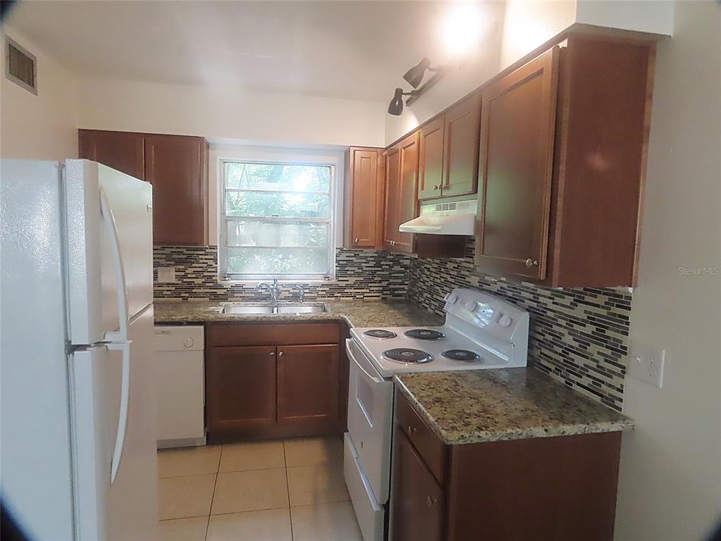 A kitchen features wood cabinets, granite countertops, a tiled backsplash, and white appliances — 1307 COOK STREET, DELAND, FL
