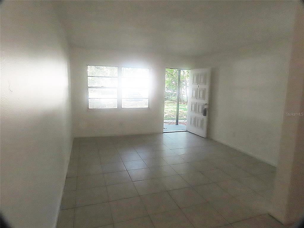 An empty room with white walls, light-colored tile flooring, large windows, and an open door — 1307 COOK STREET, DELAND, FL