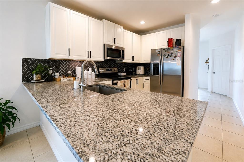 A kitchen features white cabinets, granite countertops, a stainless steel refrigerator, and a herringbone backsplash — 5003 ROYAL POINT AVENUE, KISSIMMEE, FL
