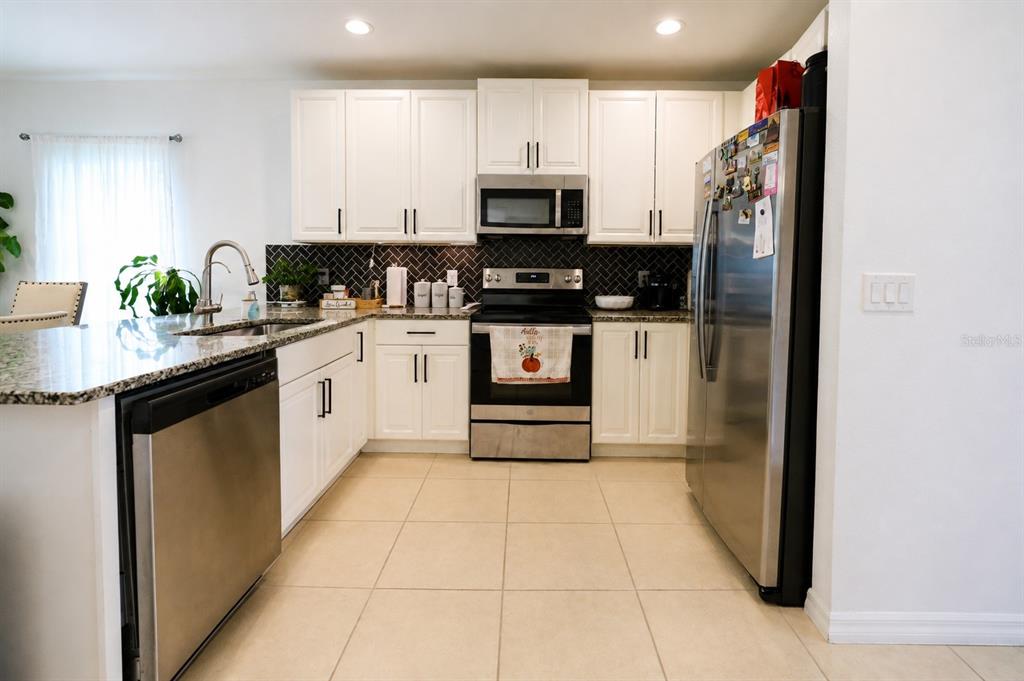 A kitchen features white cabinets, stainless steel appliances, granite countertops, and a dark herringbone backsplash — 5003 ROYAL POINT AVENUE, KISSIMMEE, FL