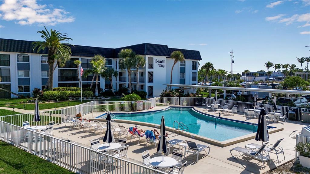 An outdoor swimming pool with lounge chairs and tables sits in front of an apartment building — 5600 BEACH WAY DRIVE UNIT 201, SARASOTA, FL