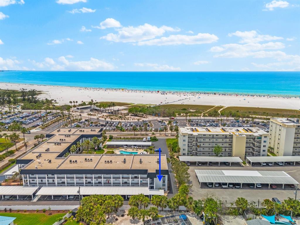 An aerial view shows a multi-story apartment building near a beach with a blue arrow — 5600 BEACH WAY DRIVE UNIT 201, SARASOTA, FL