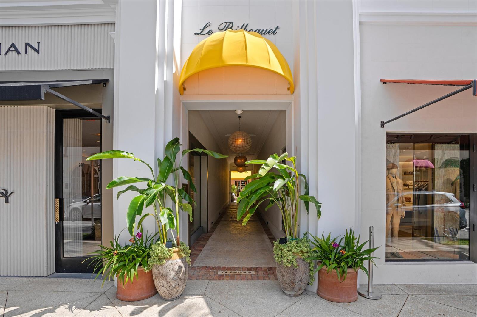An exterior view of a storefront entrance with a yellow awning and potted plants — 247 Worth Avenue, Palm Beach FL 33480, PALM BEACH, FL