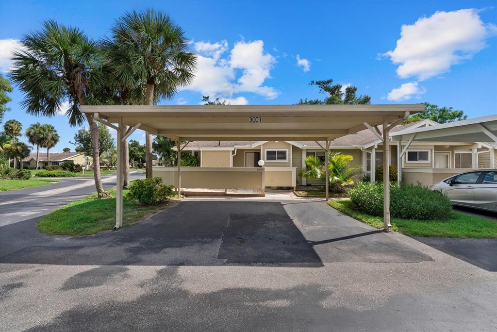 A tan single-story home features a covered carport and a paved driveway under a blue sky — 3001 SEAWIND CIRCLE UNIT 10C, VENICE, FL