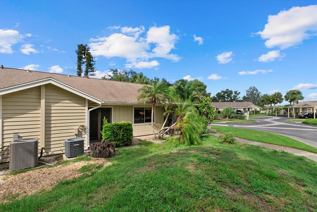 The exterior of a tan, single-story home features a lawn, palm trees, and HVAC units — 3001 SEAWIND CIRCLE UNIT 10C, VENICE, FL