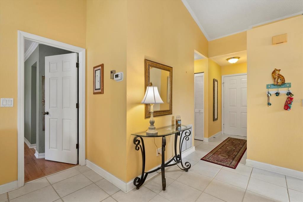 A foyer with yellow walls, tile flooring, a glass-topped console table, and a mirror — 3001 SEAWIND CIRCLE UNIT 10C, VENICE, FL