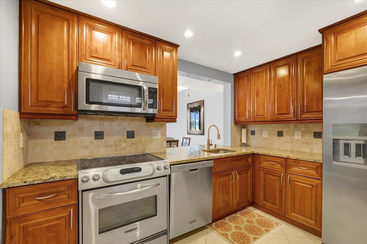A kitchen features wood cabinets, stainless steel appliances, granite countertops, and a tiled backsplash — 5190 Las Verdes Circle # 108, Delray Beach FL 33484, DELRAY BEACH, FL