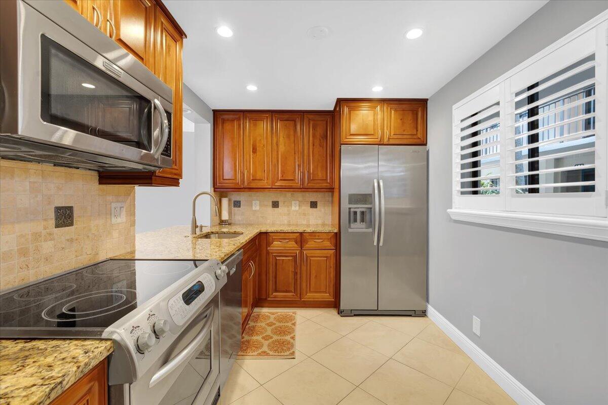 A kitchen features wood cabinets, stainless steel appliances, granite countertops, and light-colored tile flooring — 5190 Las Verdes Circle # 108, Delray Beach FL 33484, DELRAY BEACH, FL