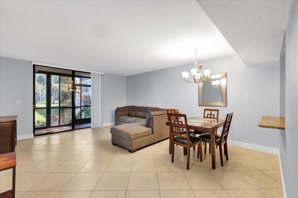 A living and dining area features light tile flooring, a grey sofa, and sliding glass doors — 5190 Las Verdes Circle # 108, Delray Beach FL 33484, DELRAY BEACH, FL