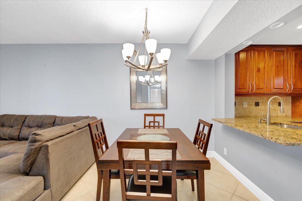 A dining area features a wooden table, chairs, a chandelier, and an adjacent kitchen counter — 5190 Las Verdes Circle # 108, Delray Beach FL 33484, DELRAY BEACH, FL