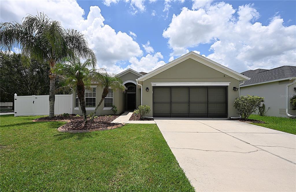 A single-story house with a beige exterior, a two-car garage, and palm trees in front — 7147 CEDARCREST BOULEVARD, LAKELAND, FL