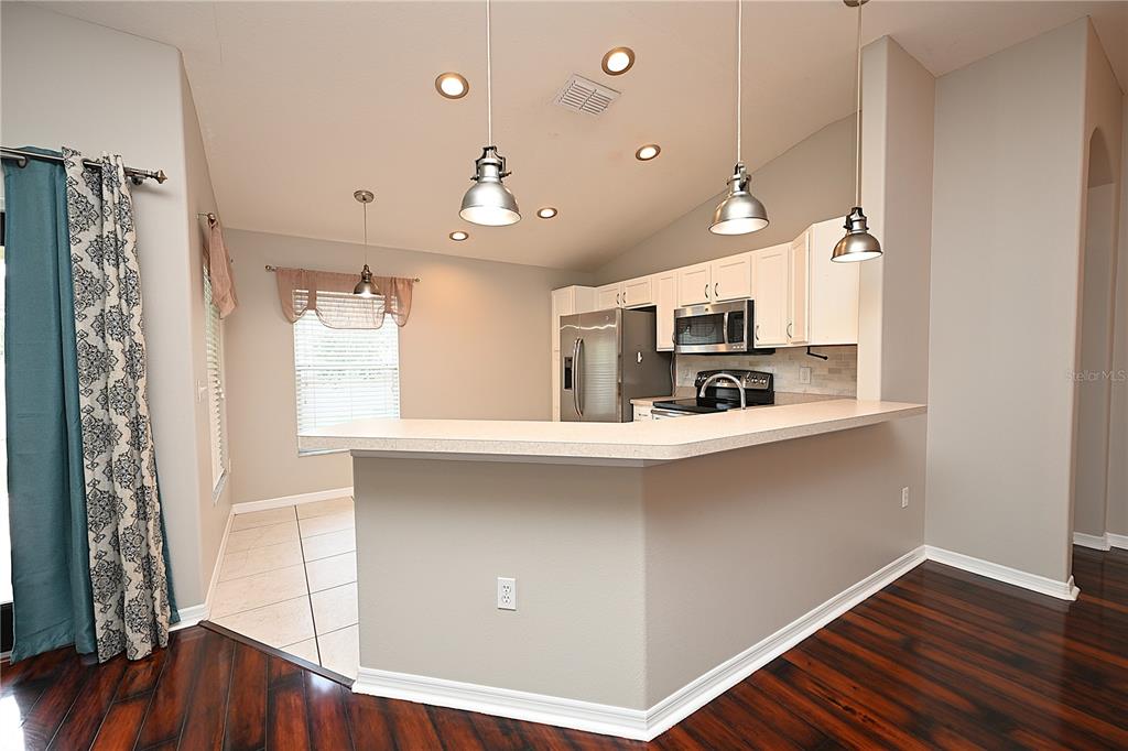 A kitchen with white cabinets, stainless steel appliances, and a breakfast bar overlooks a dining area — 7147 CEDARCREST BOULEVARD, LAKELAND, FL