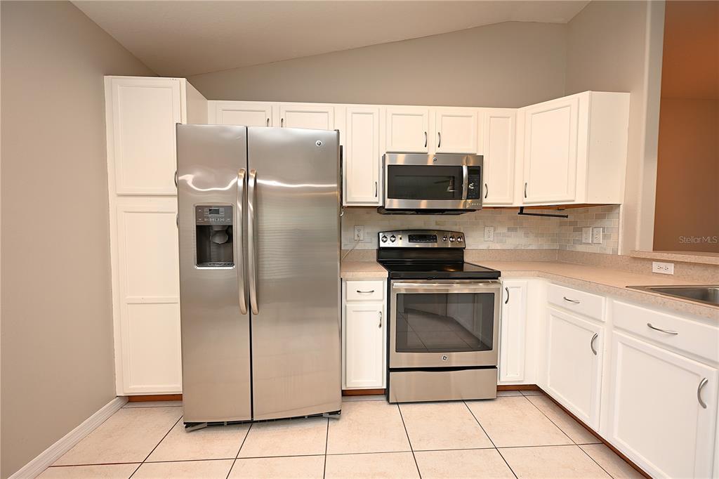 A kitchen features white cabinets, stainless steel appliances, and light-colored tile flooring — 7147 CEDARCREST BOULEVARD, LAKELAND, FL