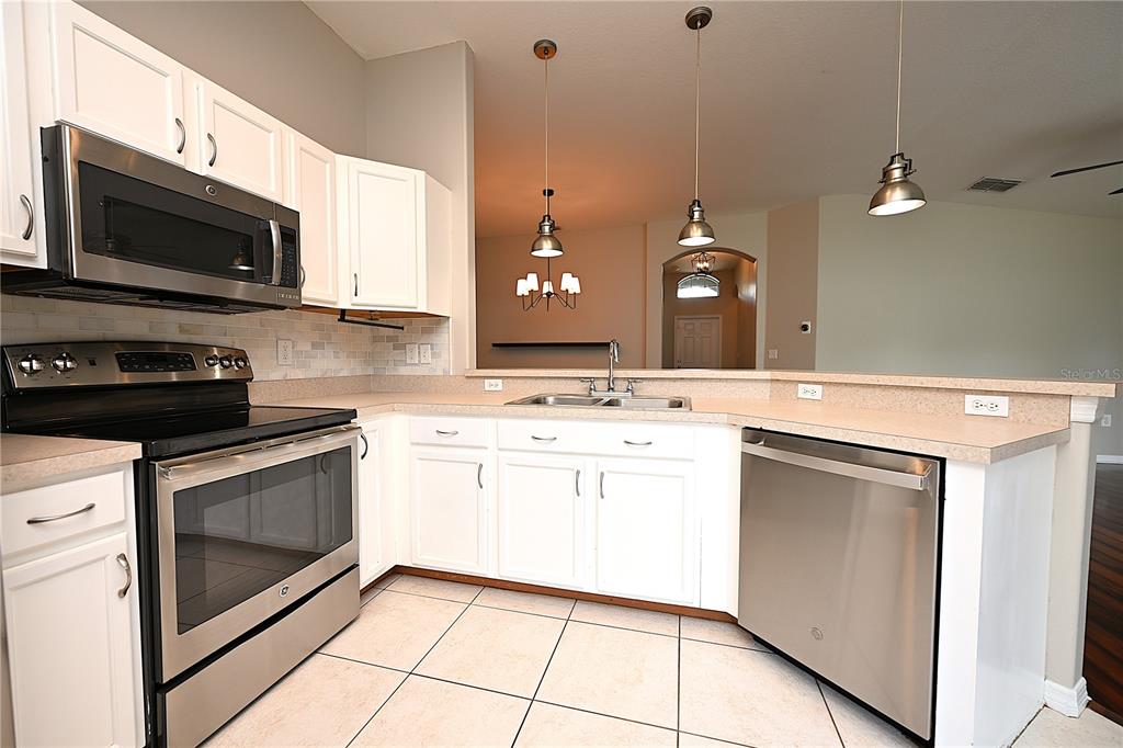 A kitchen features white cabinets, stainless steel appliances, tile flooring, and a breakfast bar — 7147 CEDARCREST BOULEVARD, LAKELAND, FL