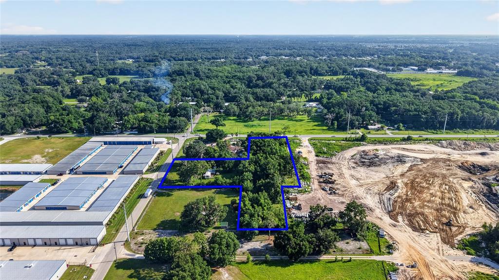 An aerial view shows a wooded property outlined in blue next to industrial storage buildings — 2919 COUNTY ROAD 523, WILDWOOD, FL