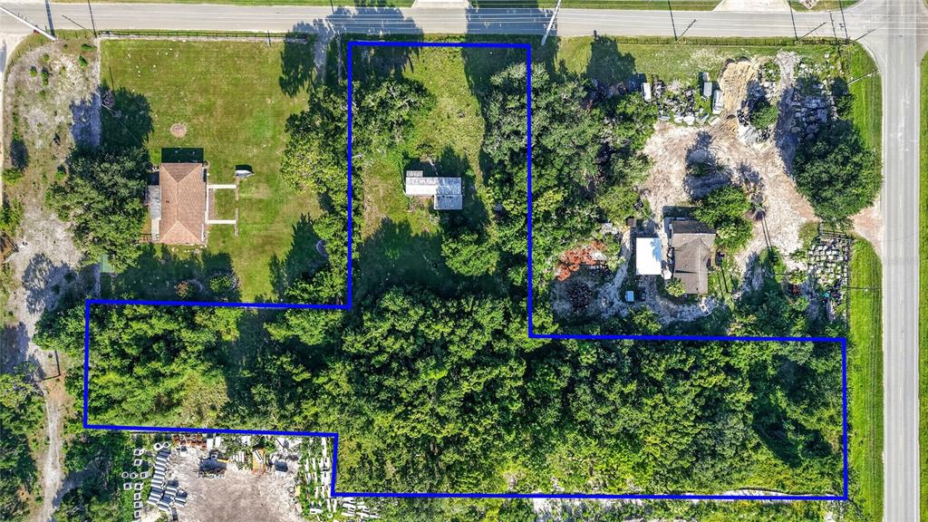This aerial view shows a large, L-shaped residential lot with trees, structures, and gravel areas — 2919 COUNTY ROAD 523, WILDWOOD, FL