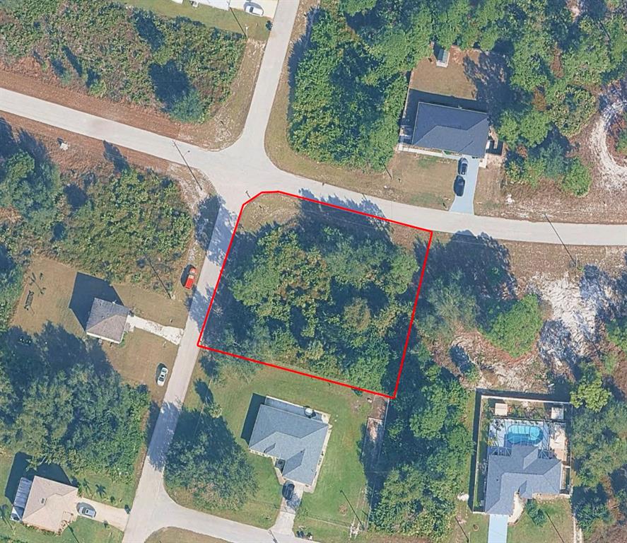 This aerial view shows a vacant, wooded corner lot outlined in red within a neighborhood — 1028 HANSEN STREET E, LEHIGH ACRES, FL