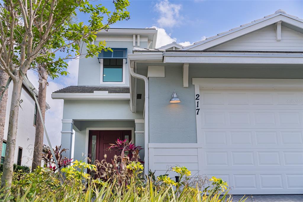 A light blue two-story house features a white garage door and a dark red door — 217 SE FASCINO CIRCLE, PORT ST LUCIE, FL