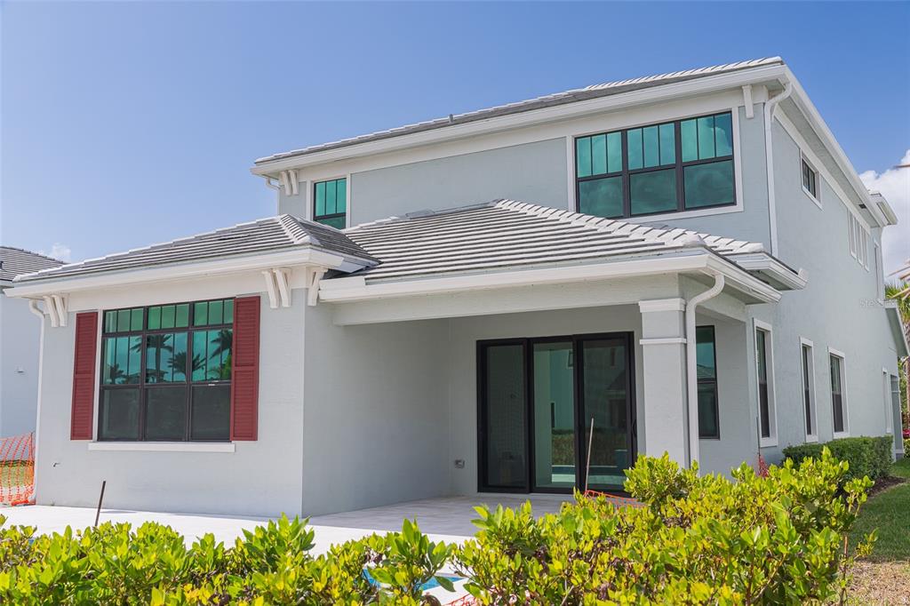 The exterior rear view of a two-story house features a patio and sliding glass doors — 217 SE FASCINO CIRCLE, PORT ST LUCIE, FL