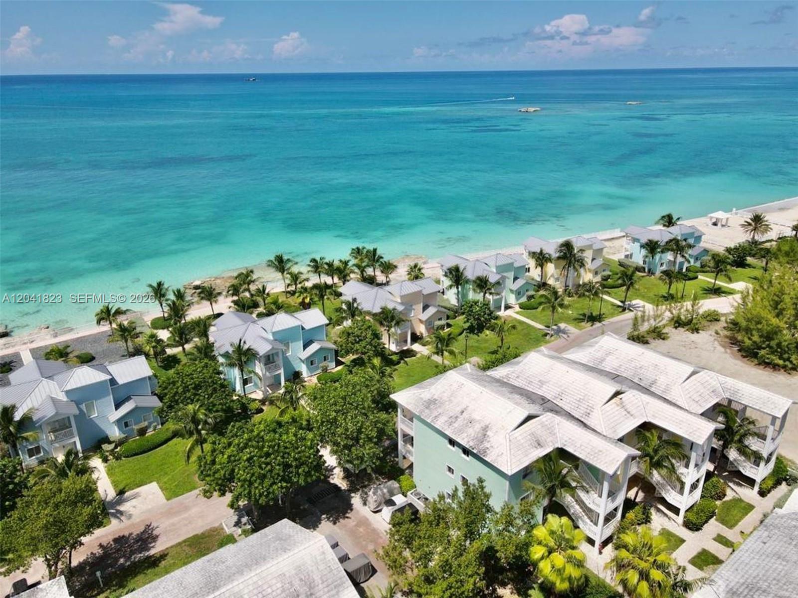 An aerial view shows multiple pastel-colored villas situated along a turquoise ocean beach — 65A Bimini Bay Resort # 302, FL, FL