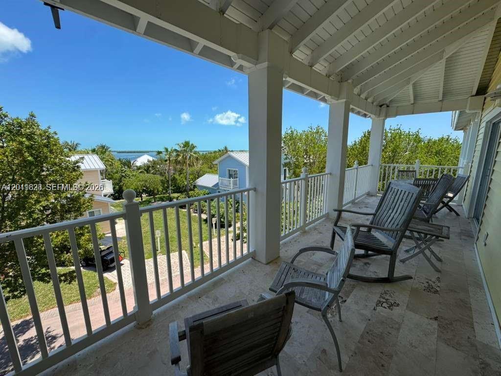 A covered balcony features stone flooring, white railings, and several wooden rocking chairs overlooking water — 65A Bimini Bay Resort # 302, FL, FL