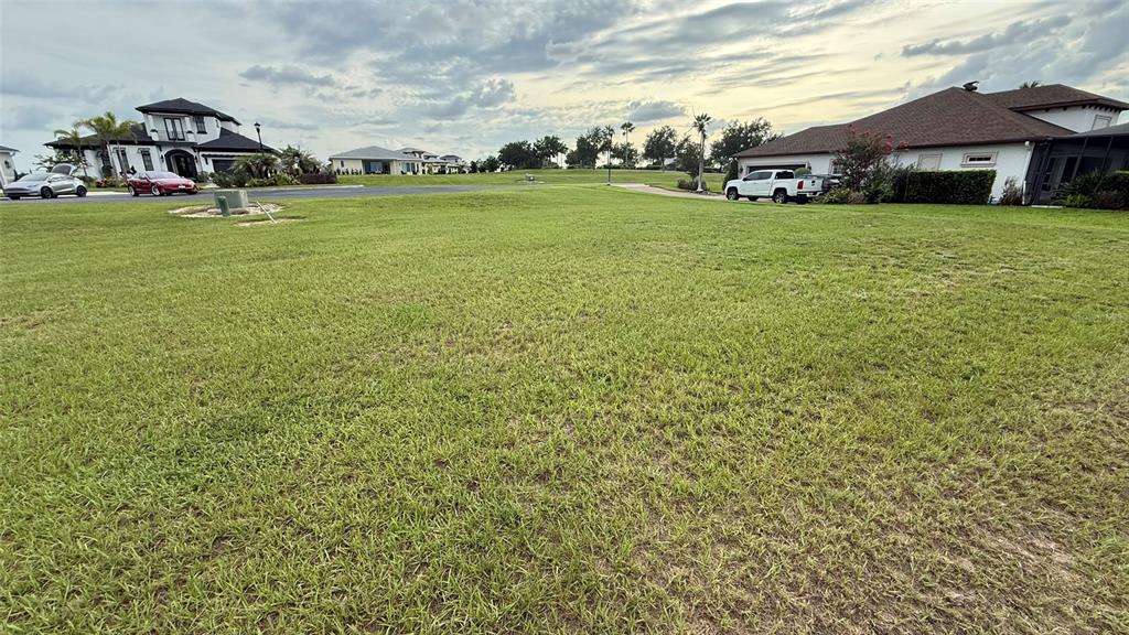 A large, grassy vacant lot sits in front of several suburban houses and parked vehicles — 210 SPRING AZURE DRIVE, LAKE ALFRED, FL