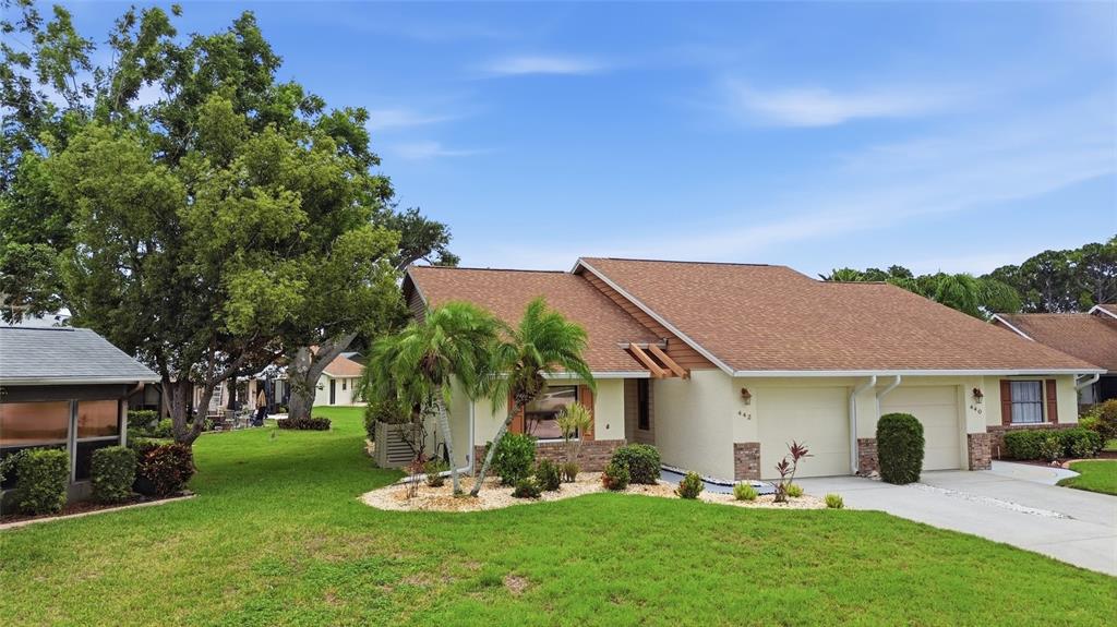 A single-story duplex with a brown shingled roof, beige stucco walls, and two garage doors — 442 PENDLETON DRIVE, VENICE, FL