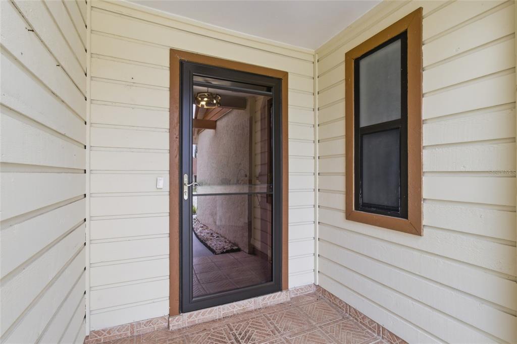 A covered entryway features light-colored horizontal siding, a dark storm door, and tiled flooring — 442 PENDLETON DRIVE, VENICE, FL