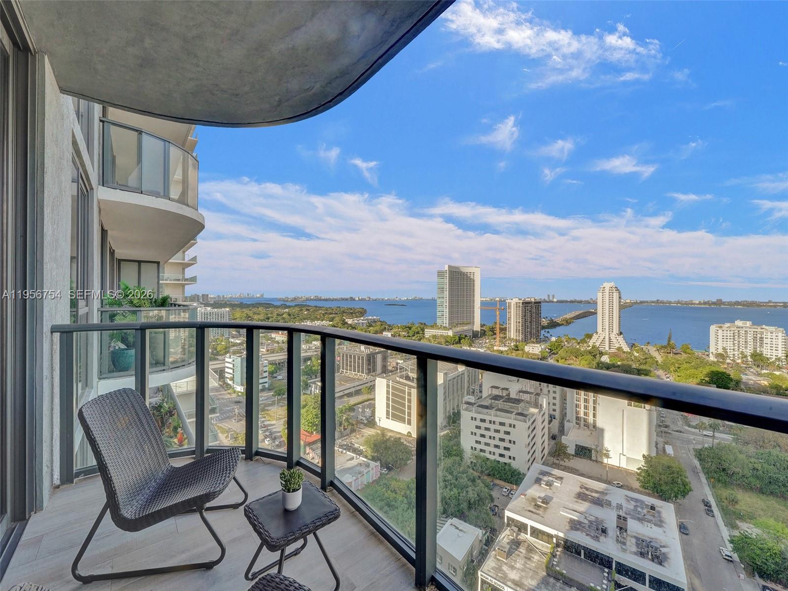 A balcony with a chair and small table overlooks a city skyline and bay — 121 NE 34th St # 2106A, Miami FL 33137, MIAMI, FL